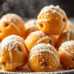Golden Oliebollen dusted with powdered sugar on rustic plate, steaming and ready to eat