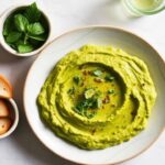 لوحة حمص هريس أخضر زستي مع رشة ليمون وخضار طازجة، طاولة مشرقة للزوار