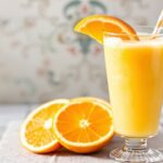 كوب عصير برتقال منزلي كريمي ومنعش بجانب كوب زجاجي، وصفة سهلة.